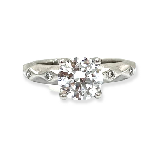 White gold diamond solitaire engagement ring with round center stone and bezel-set diamond accents along a wavy band