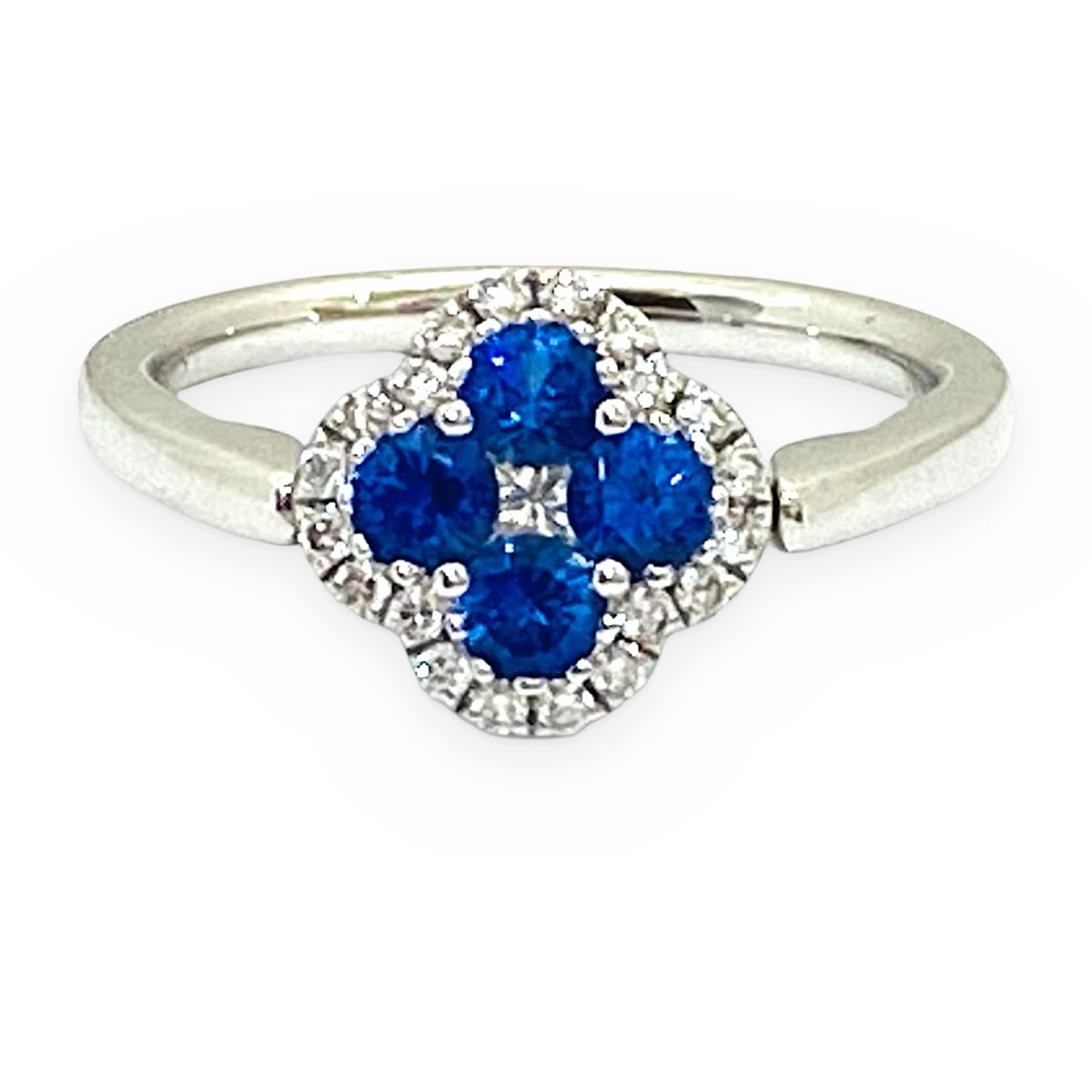 White gold clover ring with four round blue sapphires and a diamond halo