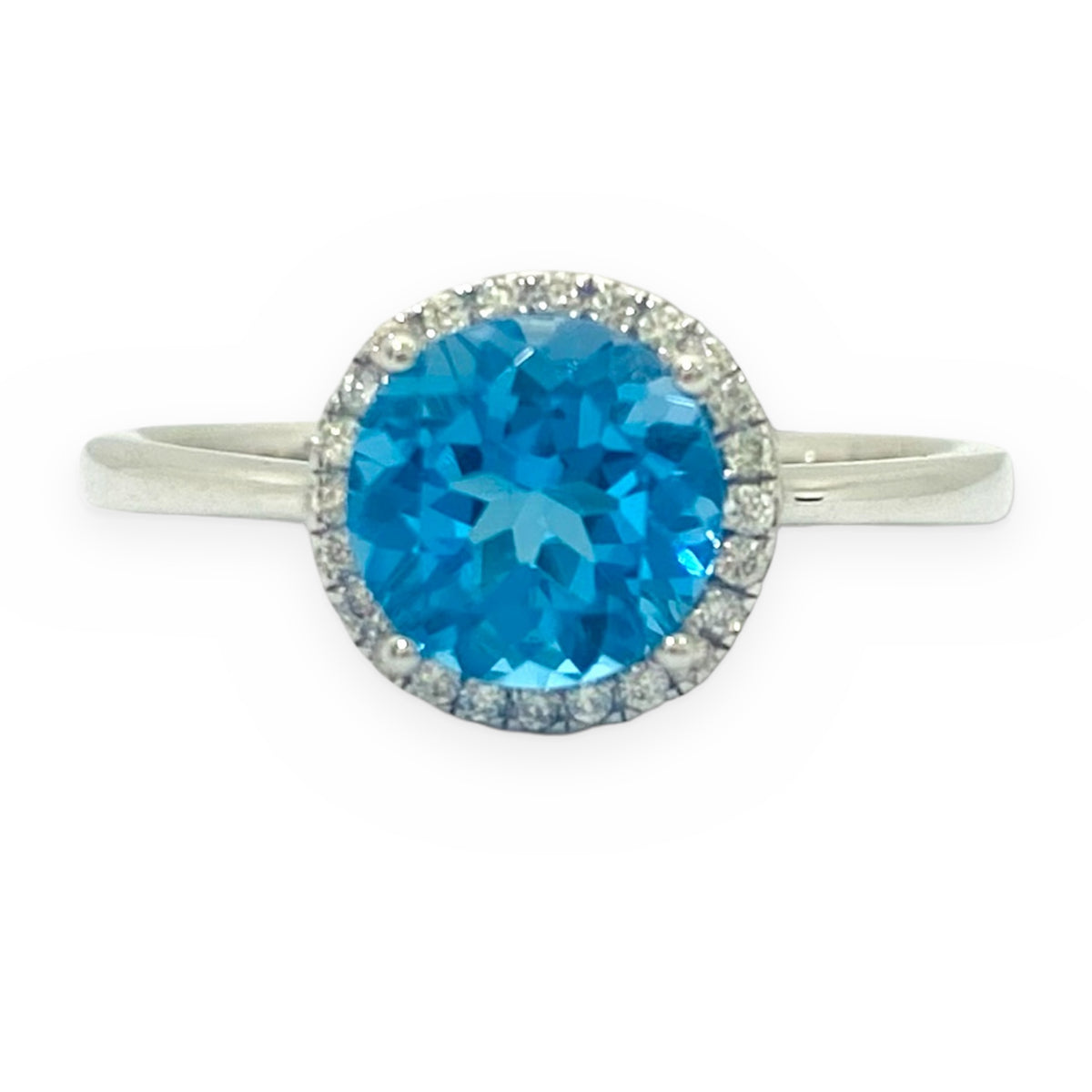 White gold ring with a round blue topaz in a diamond halo on a plain band