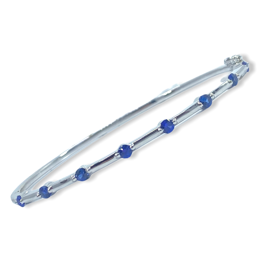 White gold thin sapphire-station bangle bracelet shown at a three-quarter angle
